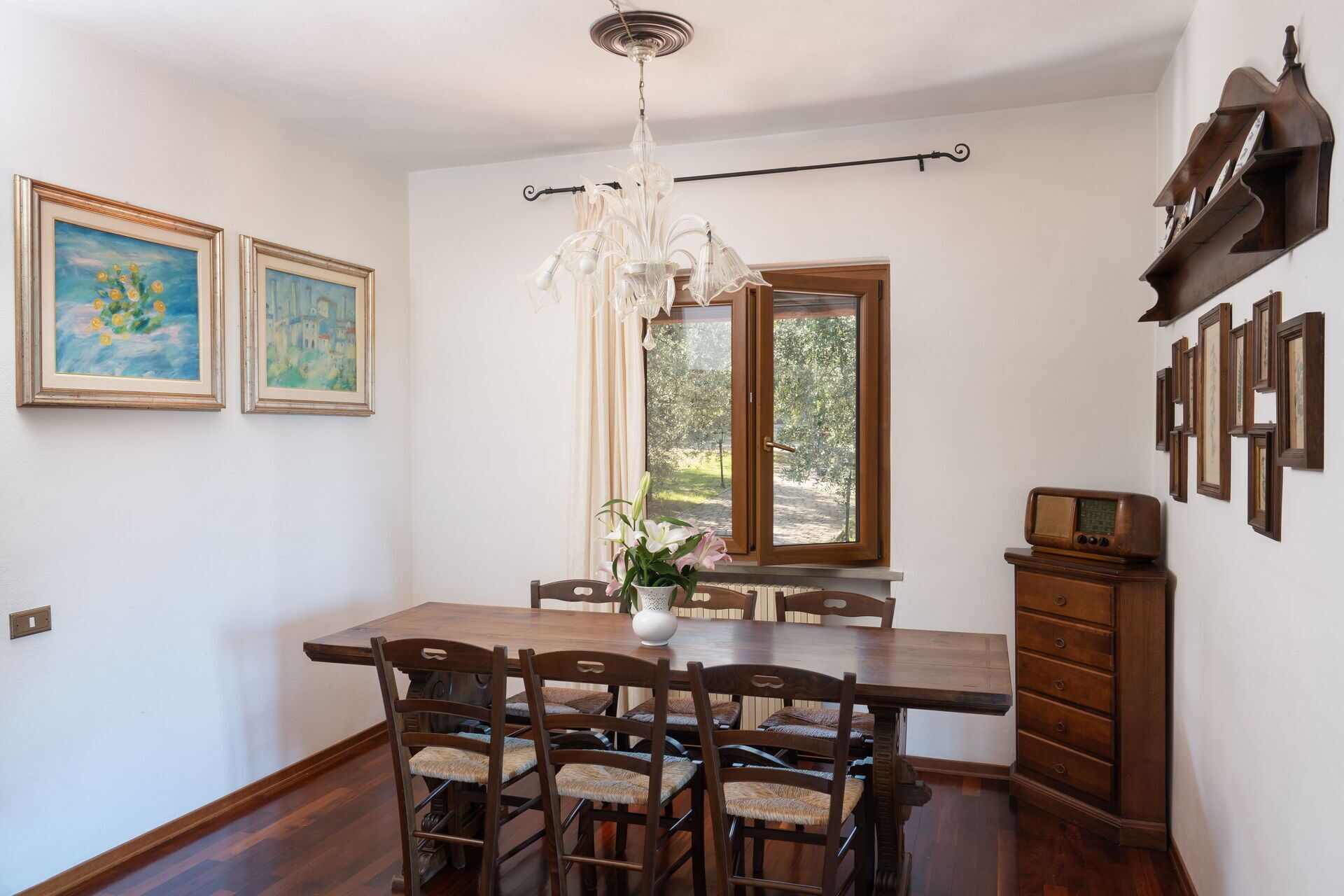 Un comedor con mesa y sillas de madera, una araña y obras de arte en las paredes.