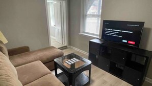 Una sala de estar con un sofá color beige, una mesa de centro de vidrio y un mueble de entretenimiento negro con un televisor de pantalla plana mostrando un mensaje.