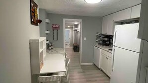 Una cocina estrecha con armarios blancos, un refrigerador y una cafetera.