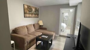 Una sala de estar con un sofá color beige, una mesa de centro negra, un televisor y un cuadro en la pared.