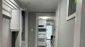 Un pasillo estrecho con un banco, una zona de cocina a lo lejos y una puerta con un cartel verde.