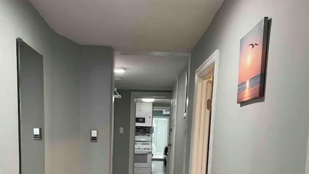 Un pasillo estrecho con suelo de madera, un banco blanco y una mesa blanca con dos tazas blancas.
