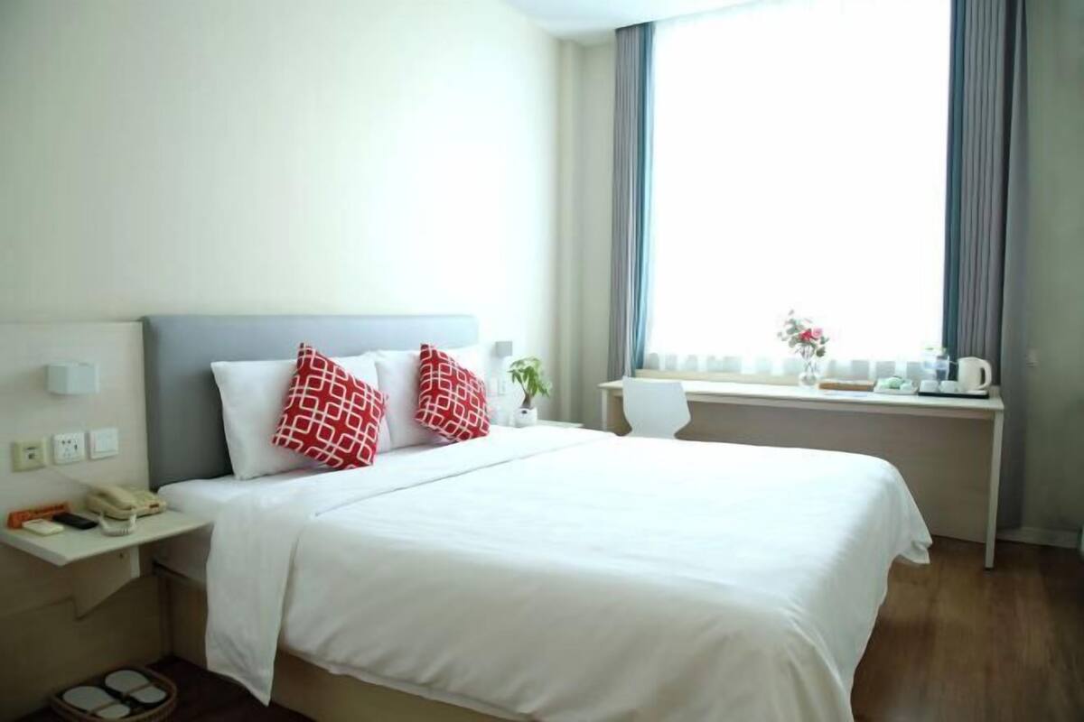 Une chambre d’hôtel avec un lit, une table de chevet et une fenêtre avec des rideaux.