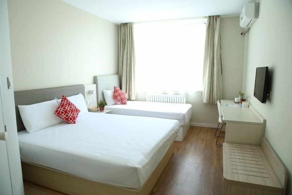 Une chambre d’hôtel avec deux lits, un bureau, une chaise, un radiateur et un téléviseur.