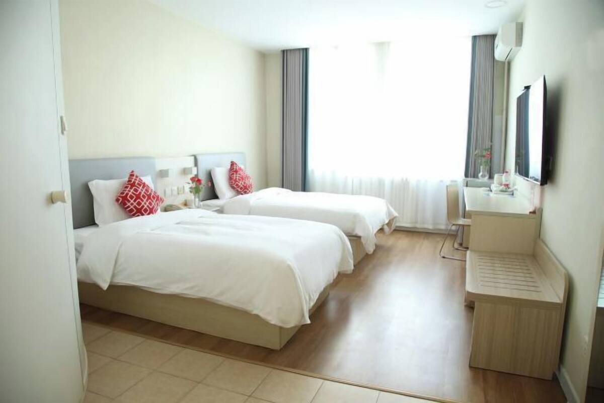 Une chambre d’hôtel avec deux lits, une table de chevet, un miroir et une fenêtre avec des rideaux.