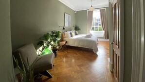Um quarto com uma cama grande, uma cadeira, uma escrivaninha e uma janela com cortinas.