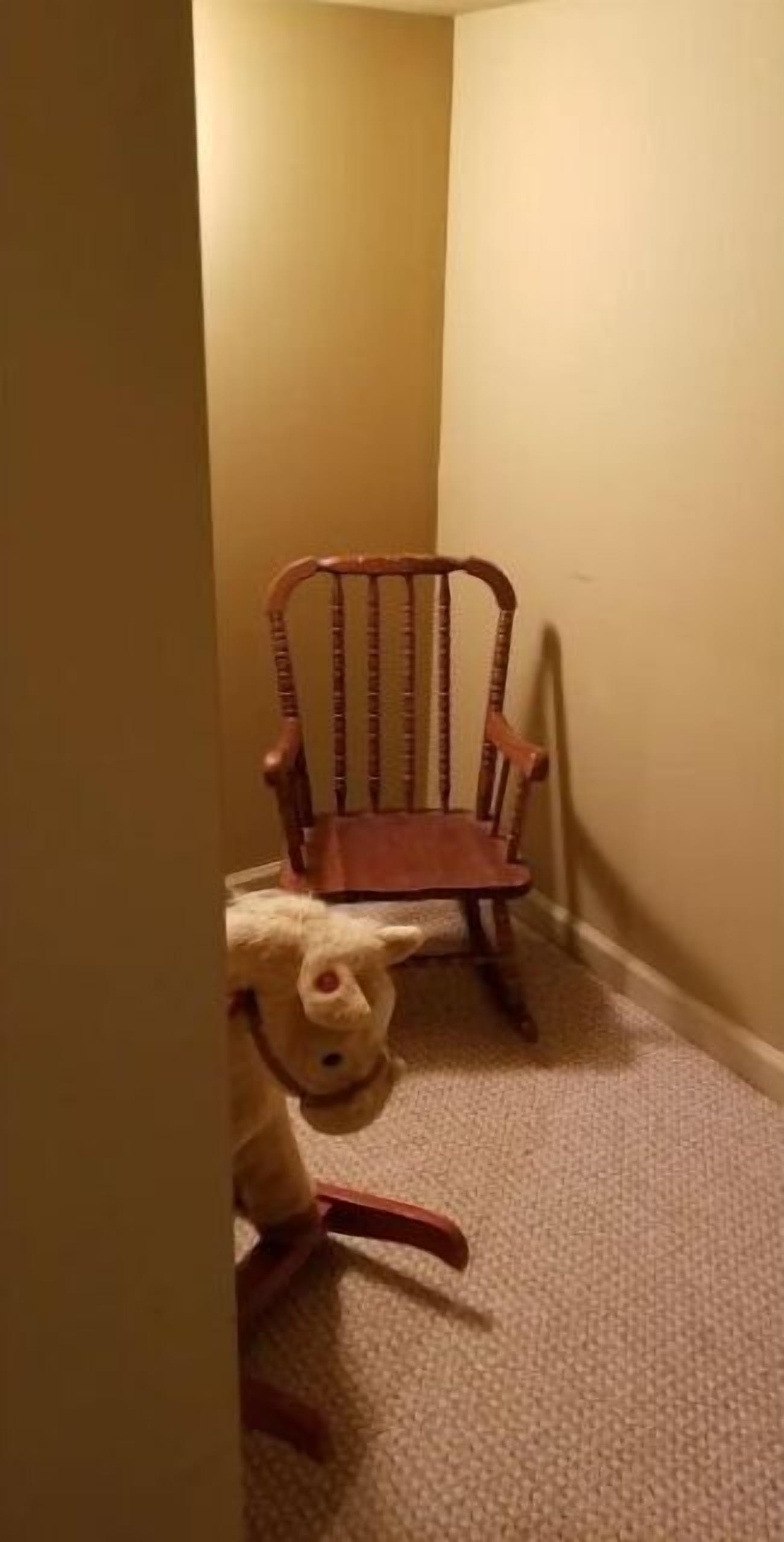 Un pasillo estrecho con una silla de madera y un oso de peluche en el suelo.