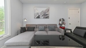 A modern living room with a sectional sofa, a glass coffee table, and a mountain landscape painting. - 5 Minutes Walk to Niagara Falls (Niagara Falls)