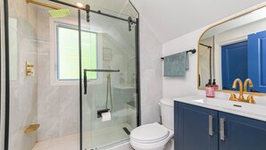 A modern bathroom with a glass-enclosed shower, a white toilet, and a blue vanity with a gold faucet. - 5 Minutes Walk to Niagara Falls (Niagara Falls)