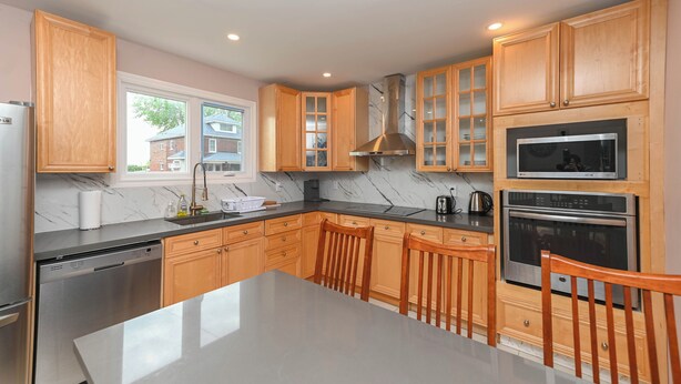 A modern kitchen with wooden cabinets, a stainless steel dishwasher, a marble countertop, and a large island with chairs. - 5 Minutes Walk to Niagara Falls (Niagara Falls)