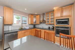 A modern kitchen with wooden cabinets, a stainless steel dishwasher, a marble countertop, and a large island with chairs. - 5 Minutes Walk to Niagara Falls (Niagara Falls)