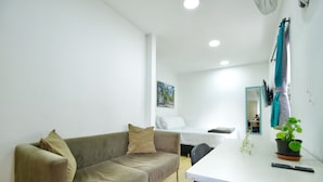 A modern, well-lit room with a sofa, a small table with a plant, and a bed in the background. - Poblado Park Guest House (Medellín)