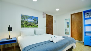 A hotel room with a bed, a nightstand, a blue desk, a wooden wardrobe, and a painting on the wall. - Poblado Park Guest House (Medellín)