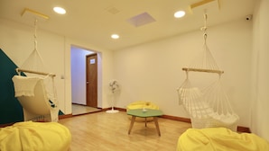 A room with wooden flooring, two hanging hammocks, a green table, and two yellow bean bags. - Poblado Park Guest House (Medellín)