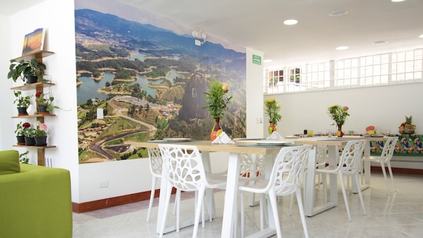 A dining area with a large mural, white chairs, a green sofa, and potted plants. - Poblado Park Guest House (Medellín)