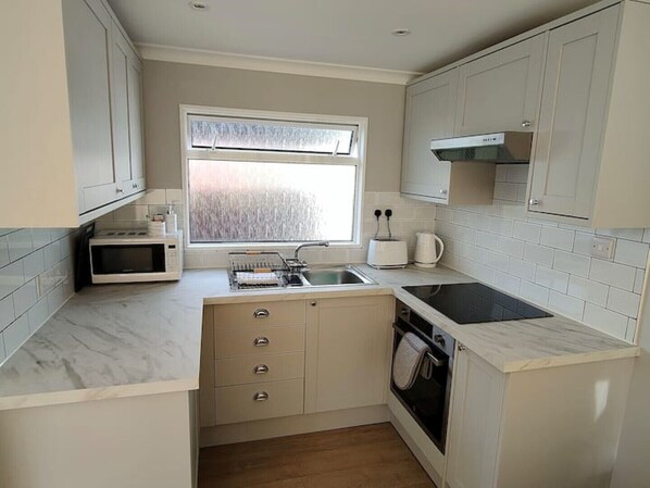 A compact kitchen with white cabinets, a microwave, a toaster, a sink, and a stove. - Holiday chalet in Selsey (Selsey)