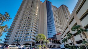 A high-rise hotel with multiple floors, a central glass building, and a parking area with cars. - Beautiful Ocean Front Margate Tower 4 Bedroom Condo (Myrtle Beach)