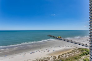 A beach with a pier extending into the ocean, a sandy beach, and a high-rise building on the right.