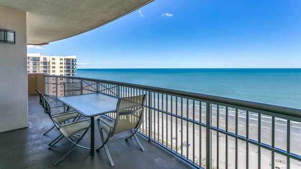 A balcony with a table and chairs, overlooking a beach and ocean. - Beautiful Ocean Front Margate Tower 4 Bedroom Condo (Myrtle Beach)