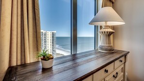 A view from a window with a lamp and a plant on a wooden dresser, overlooking a beach and high-rise buildings. - Beautiful Ocean Front Margate Tower 4 Bedroom Condo (Myrtle Beach)