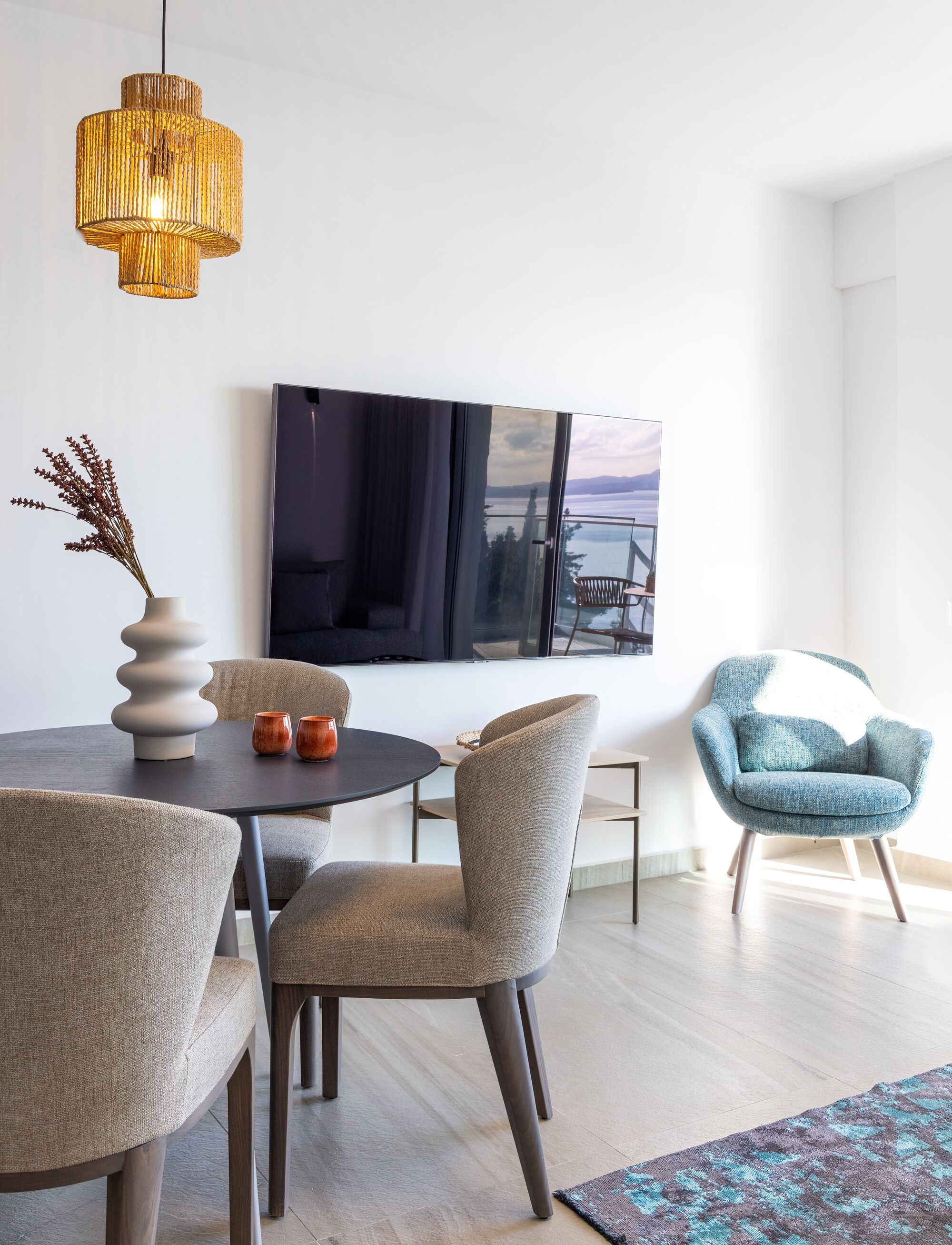 A modern dining area with a round table, chairs, a vase, and a hanging light fixture.
