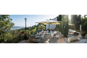 Area patio esterna con tavoli e sedie, circondata da vegetazione e con vista sul paesaggio.