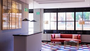 A modern lobby with a reception desk, a red sofa, and a patterned floor. - THE Apartment by Assethoteles (Torrejón de Ardoz)