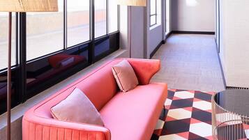 Un vestíbulo de hotel moderno con un sofá rosa, un suelo de estampado geométrico y grandes ventanales.