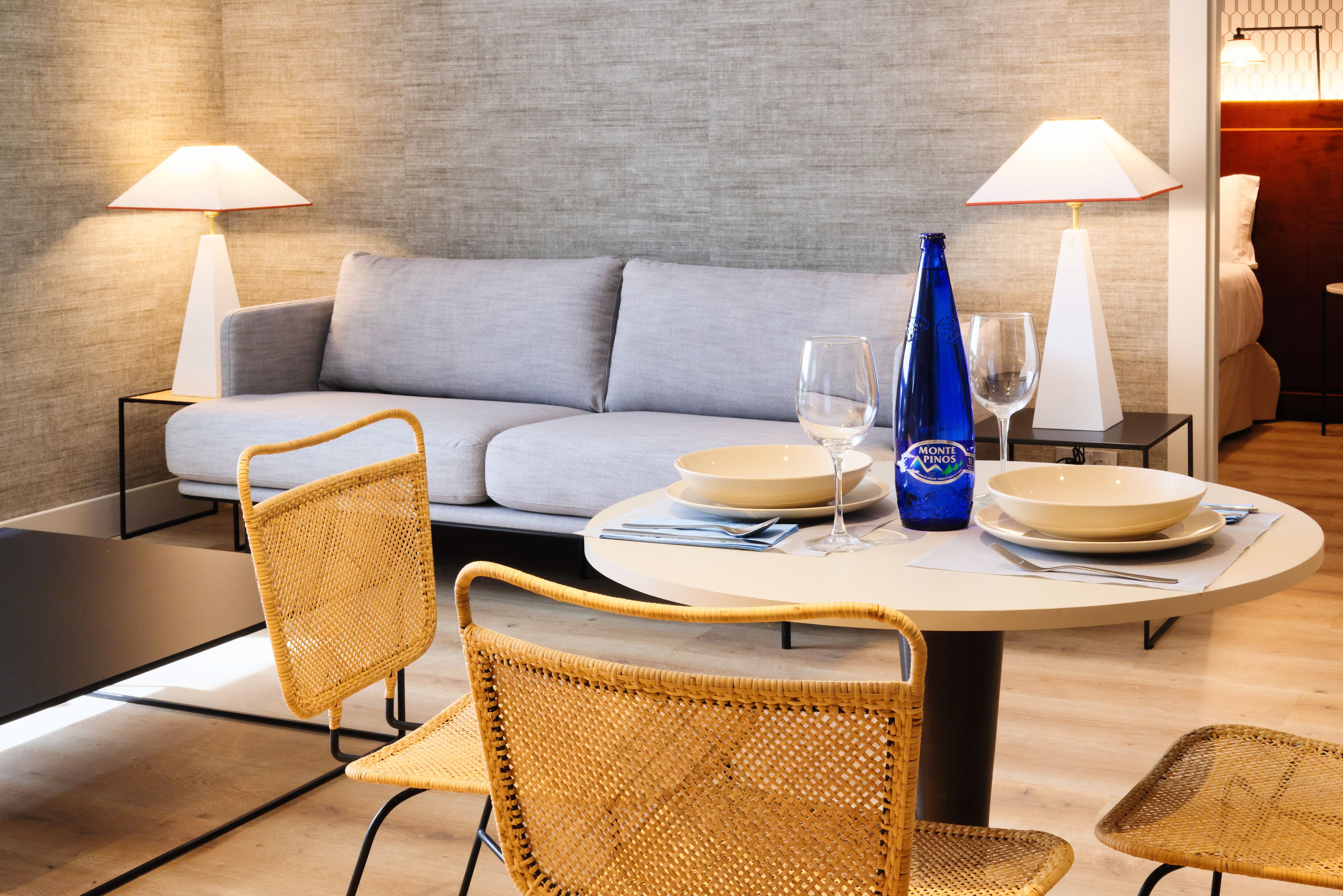 A dining area with a round table, two chairs, a sofa, and two lamps.