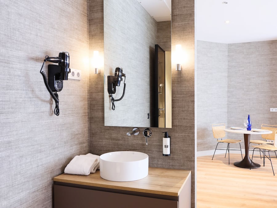 A modern bathroom with a large mirror, two hair dryers, a sink, and a towel.