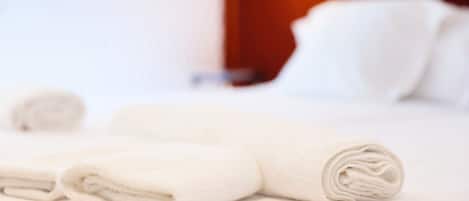 A neatly made bed with white linens and pillows, a wooden headboard, and a window with daylight coming through.
