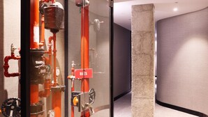 A modern interior with a glass partition displaying industrial-style red pipes and valves, a concrete pillar, and a curved wall. - THE Apartment by Assethoteles (Torrejón de Ardoz)