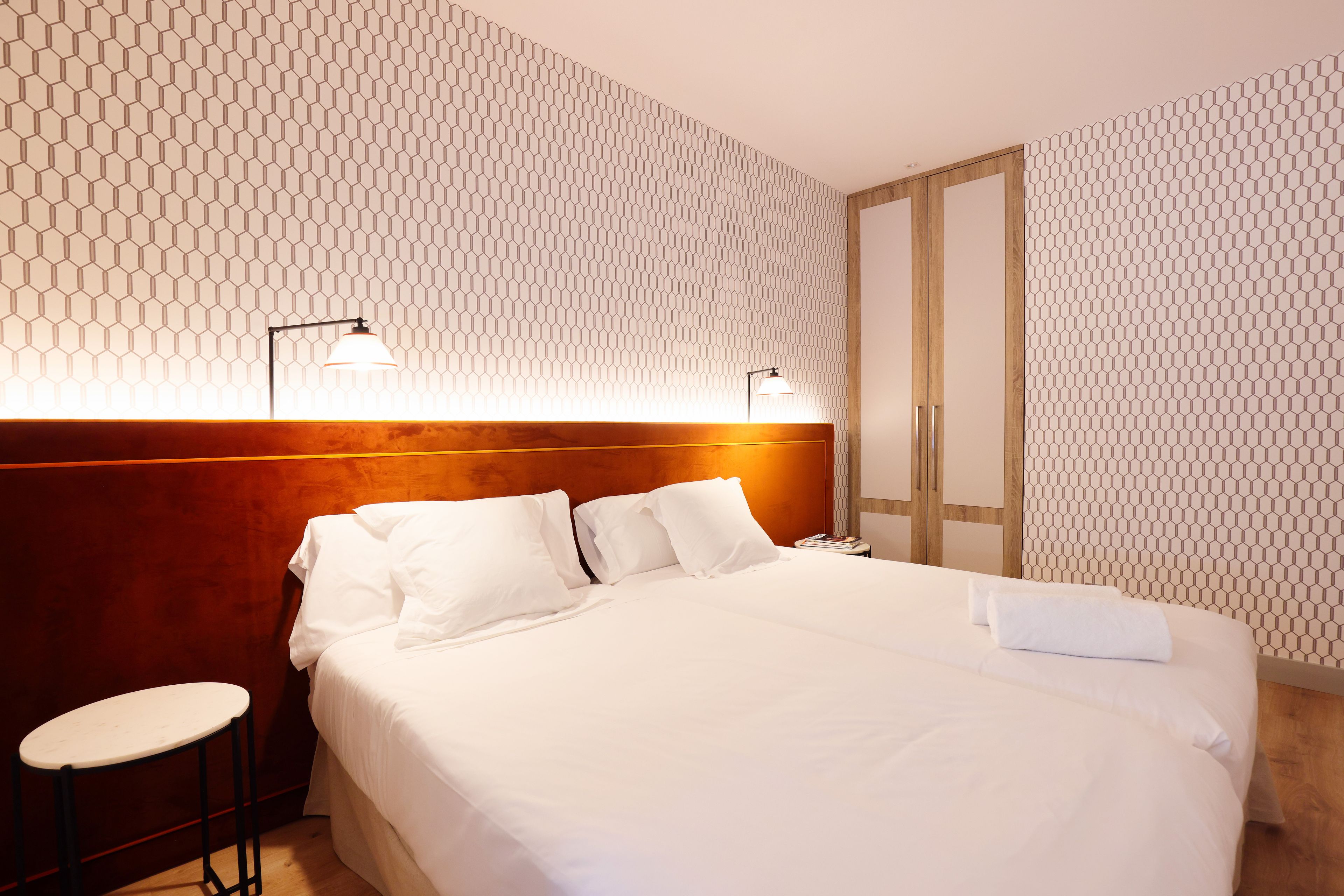 Habitación de hotel con una cama grande, dos lámparas de noche, un cabecero de madera, una mesita y un armario.