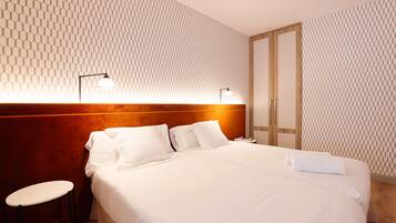 Habitación de hotel con una cama grande, dos lámparas de noche, un cabecero de madera, una mesita y un armario.