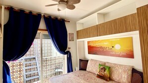 Ein Schlafzimmer mit Bett, Deckenventilator, Blick ins Freie und einem motivierenden Zitat an der Wand.