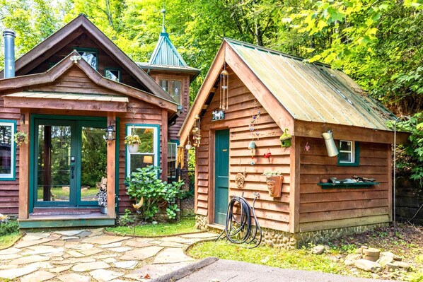 Un chalet rustique avec un sentier de pierres menant à l’entrée, une petite véranda et une cheminée.