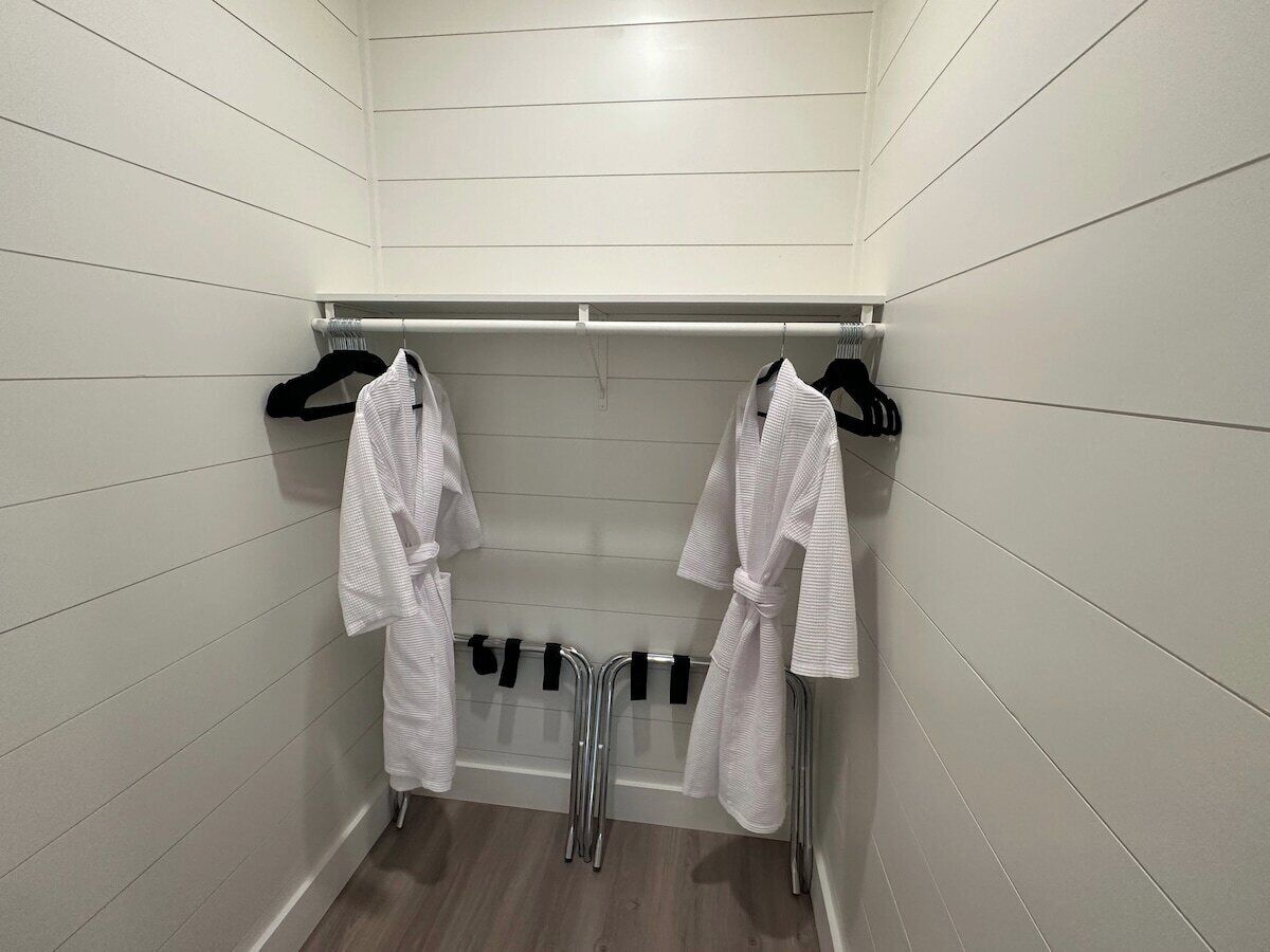 A bathroom with two white robes hanging on a rack, a shower area, and a wooden floor.