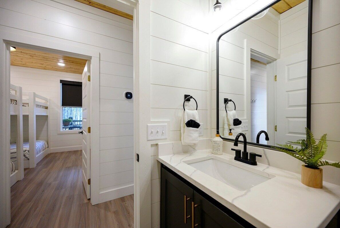 A modern bathroom with a white and black color scheme, a large mirror, and a sink with a plant on the counter.