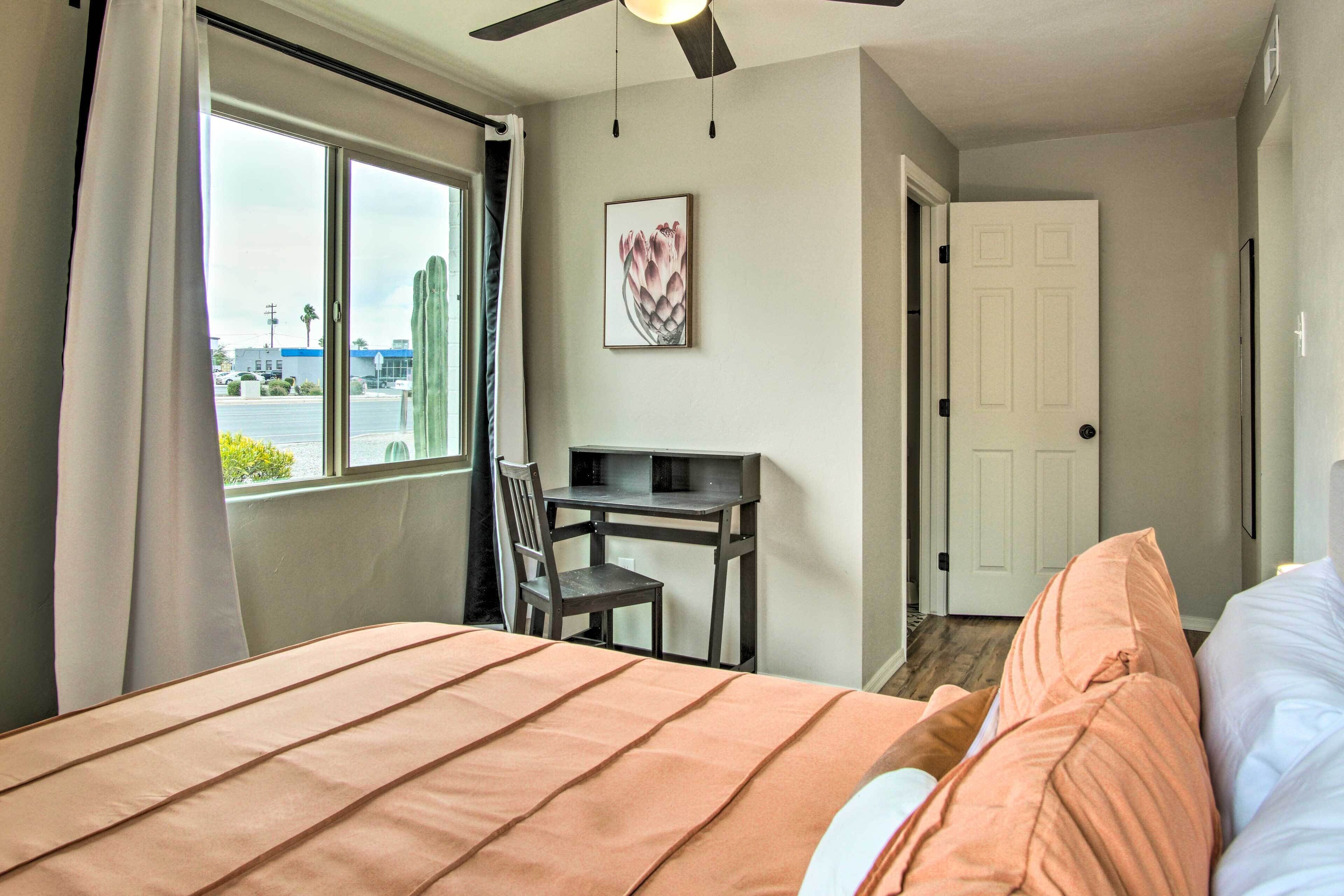 Un dormitorio con cama, escritorio, silla, ventana con cortinas y puerta.