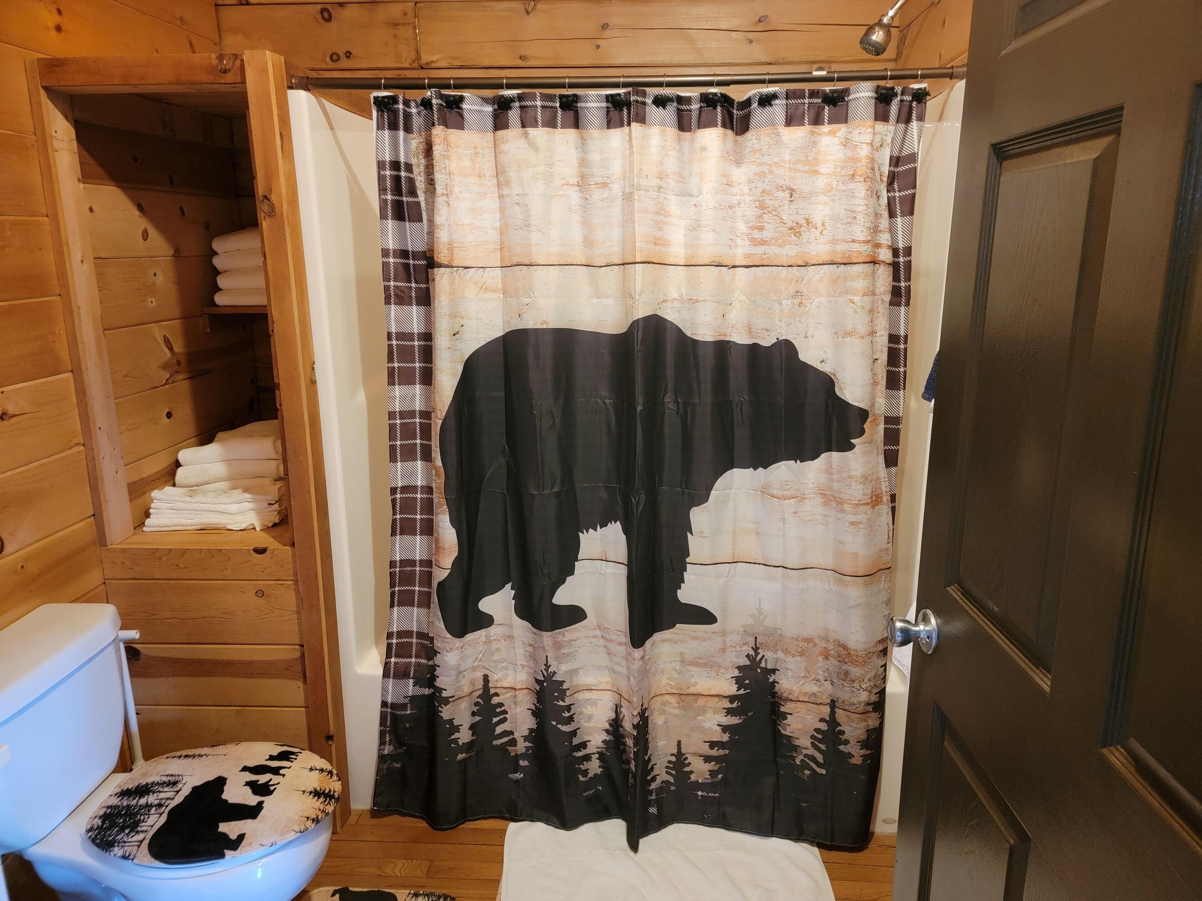 A bathroom with a wooden interior, a toilet with a bear-themed seat cover, and a shower curtain with a bear silhouette.