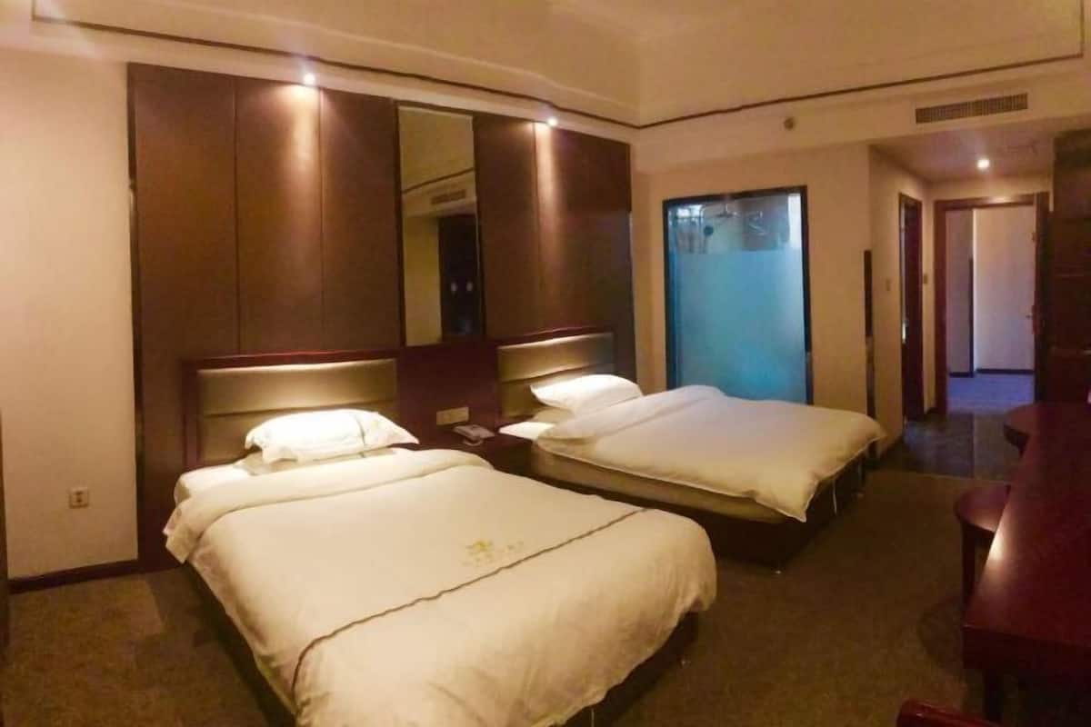Une chambre d’hôtel avec deux lits, un grand miroir et une porte donnant sur une autre pièce.
