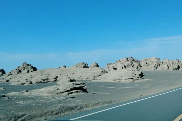 A desert landscape with a paved road, rocky formations, and a clear blue sky. - Jiulong Holiday Hotel (Hami)