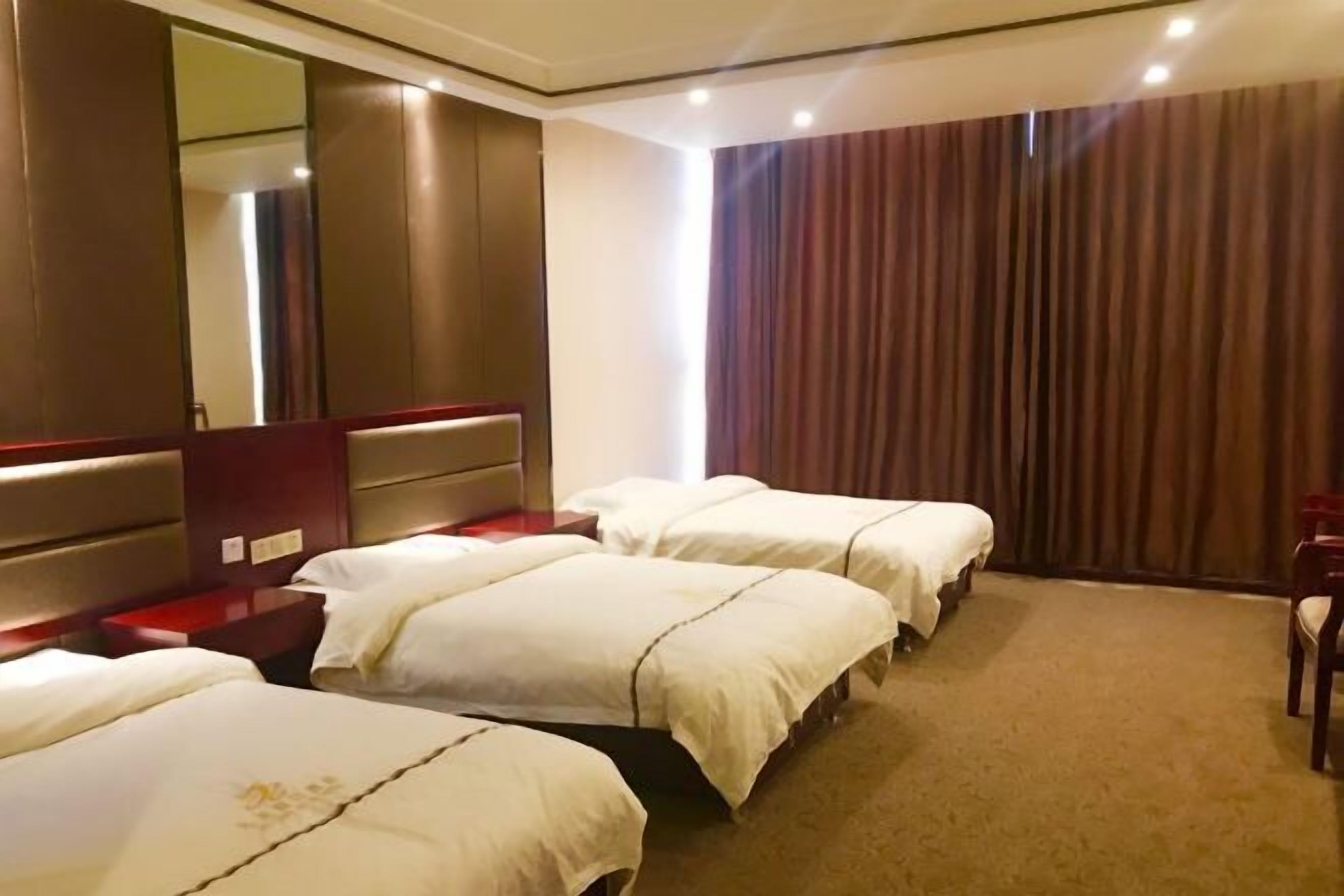 Habitación de hotel con tres camas, un espejo grande, una pared de acento roja y vista al exterior.