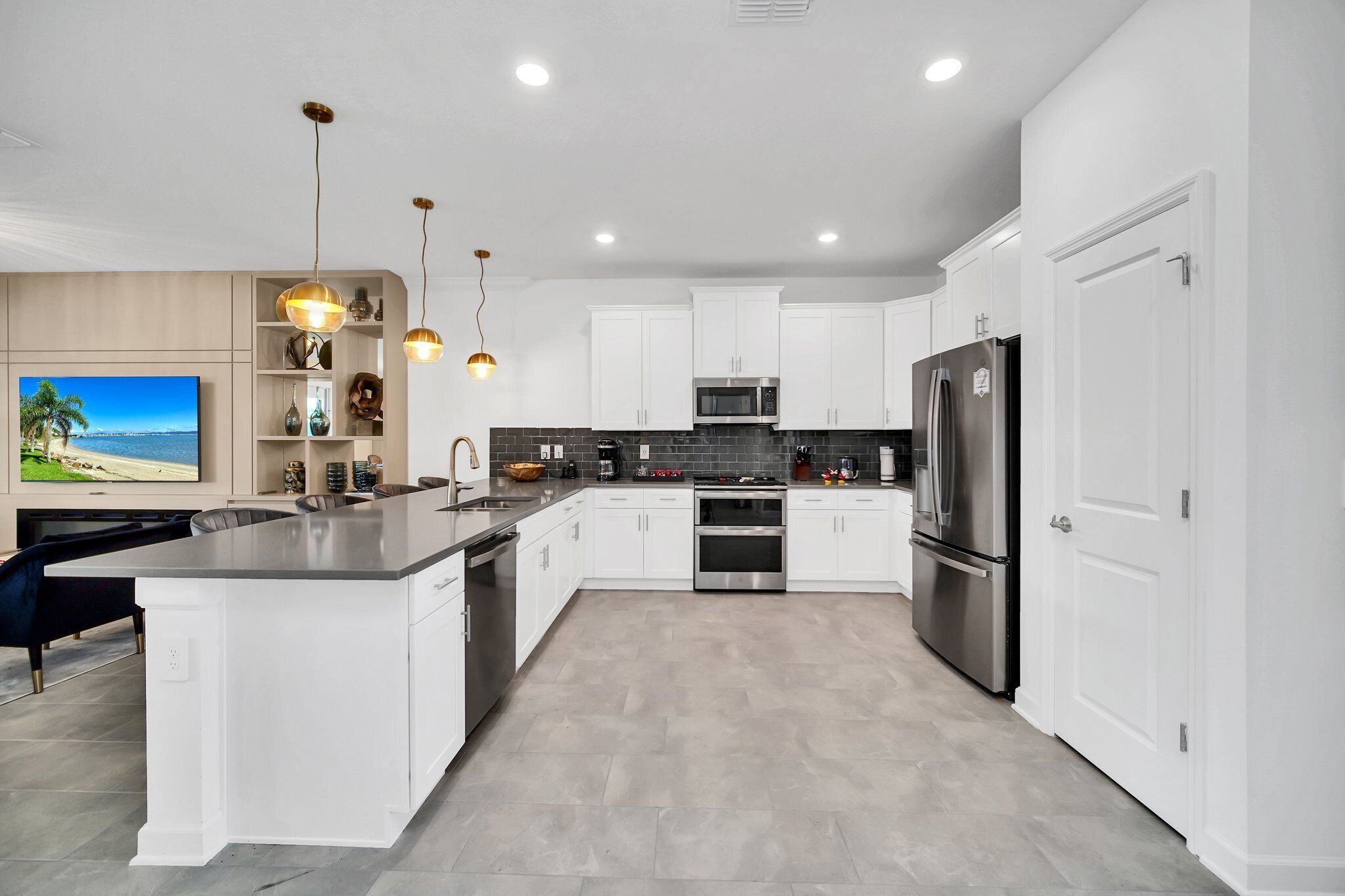 A modern kitchen with white cabinetry, a stainless steel refrigerator, and a large island with a sink.