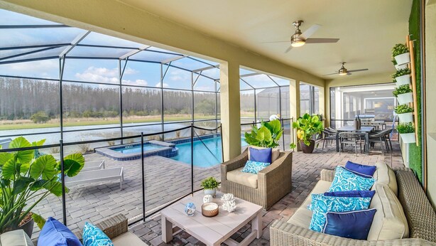Une terrasse extérieure couverte avec une piscine, des meubles en osier et des plantes en pot.