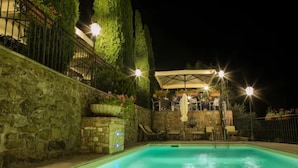 Una piscina con una parete in pietra e una zona relax coperta con ombrelloni.