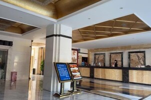 A hotel lobby with a reception desk, a large pillar, and a blue informational sign.