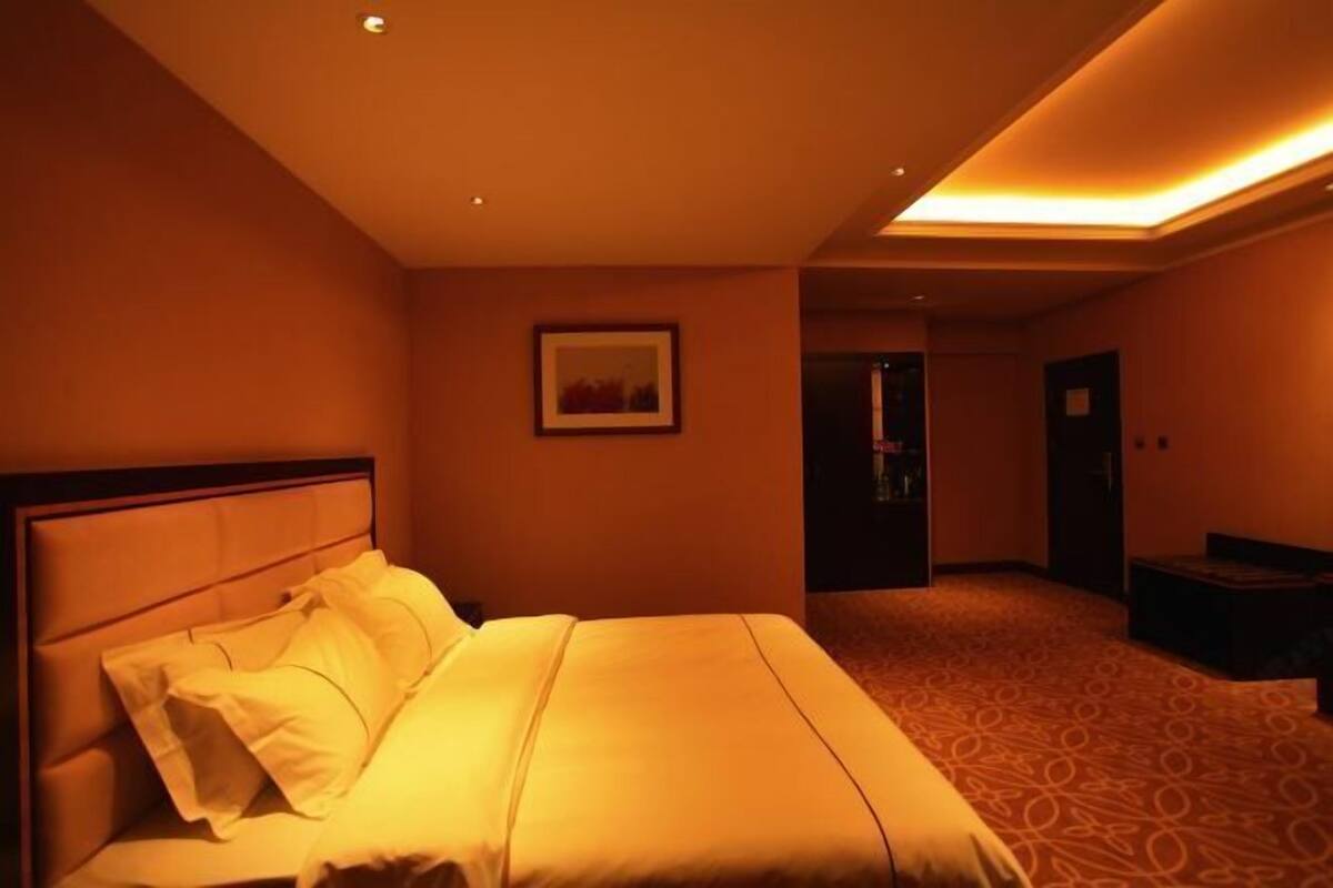 Ein Hotelzimmer mit einem Bett, einem gerahmten Bild an der Wand und einer Tür zu einem anderen Raum.