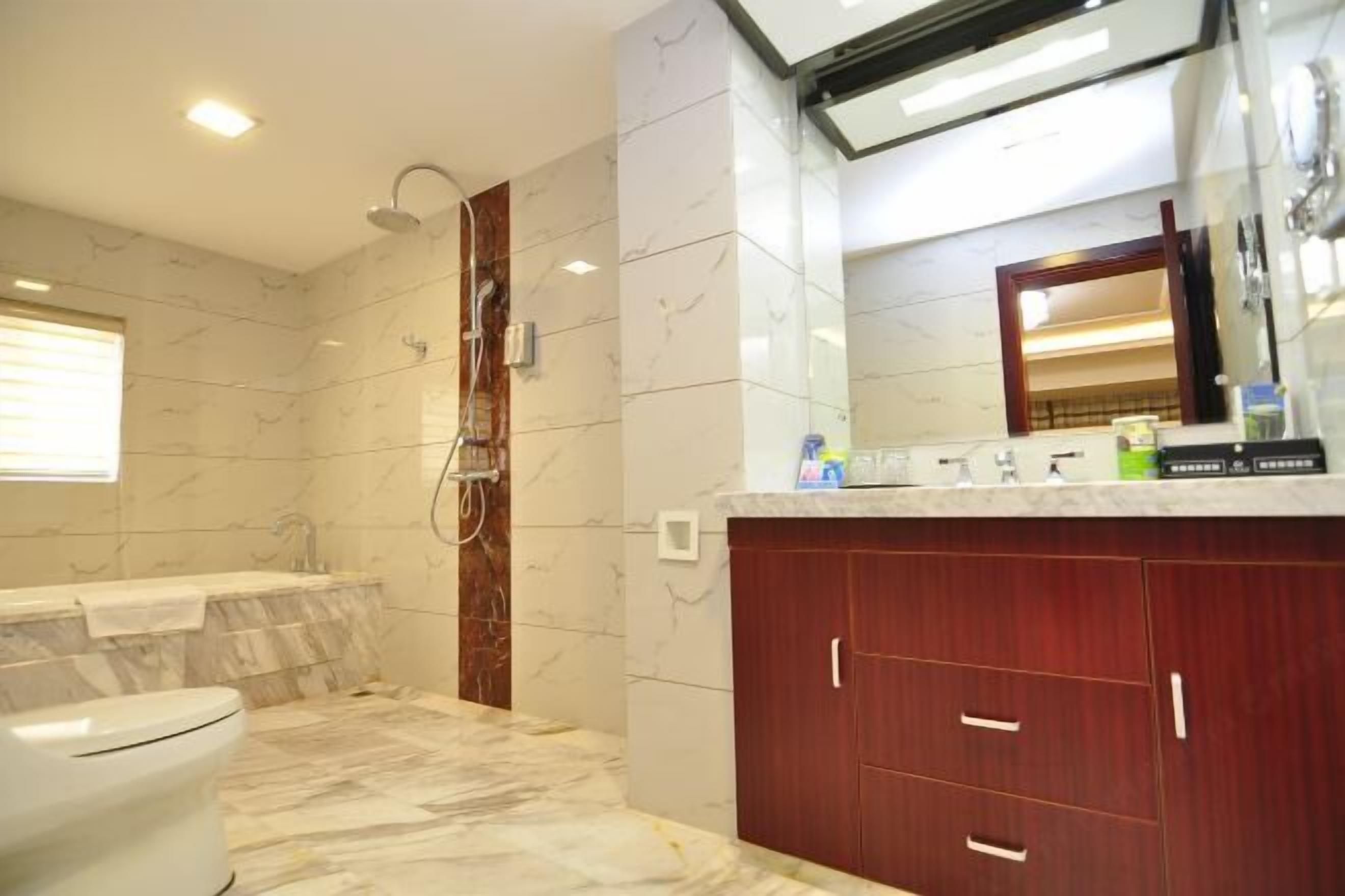 Un baño con ducha, inodoro, tocador con espejo y suelo de mármol.