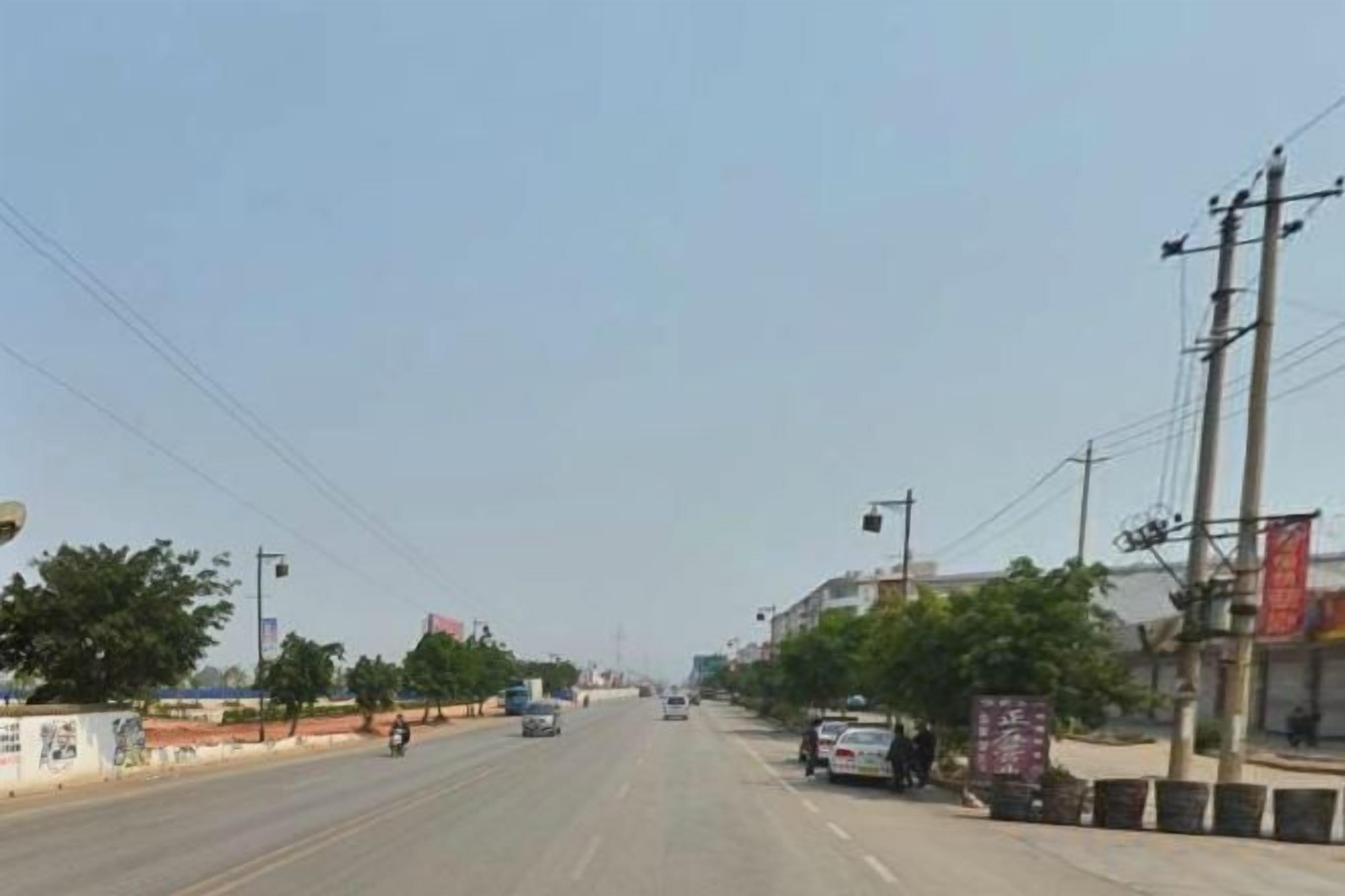 Una carretera con varios carriles, vehículos, líneas eléctricas y edificios a la derecha.